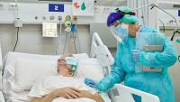 Female Doctor Supporting Male Patient Lying in Hospital Bed